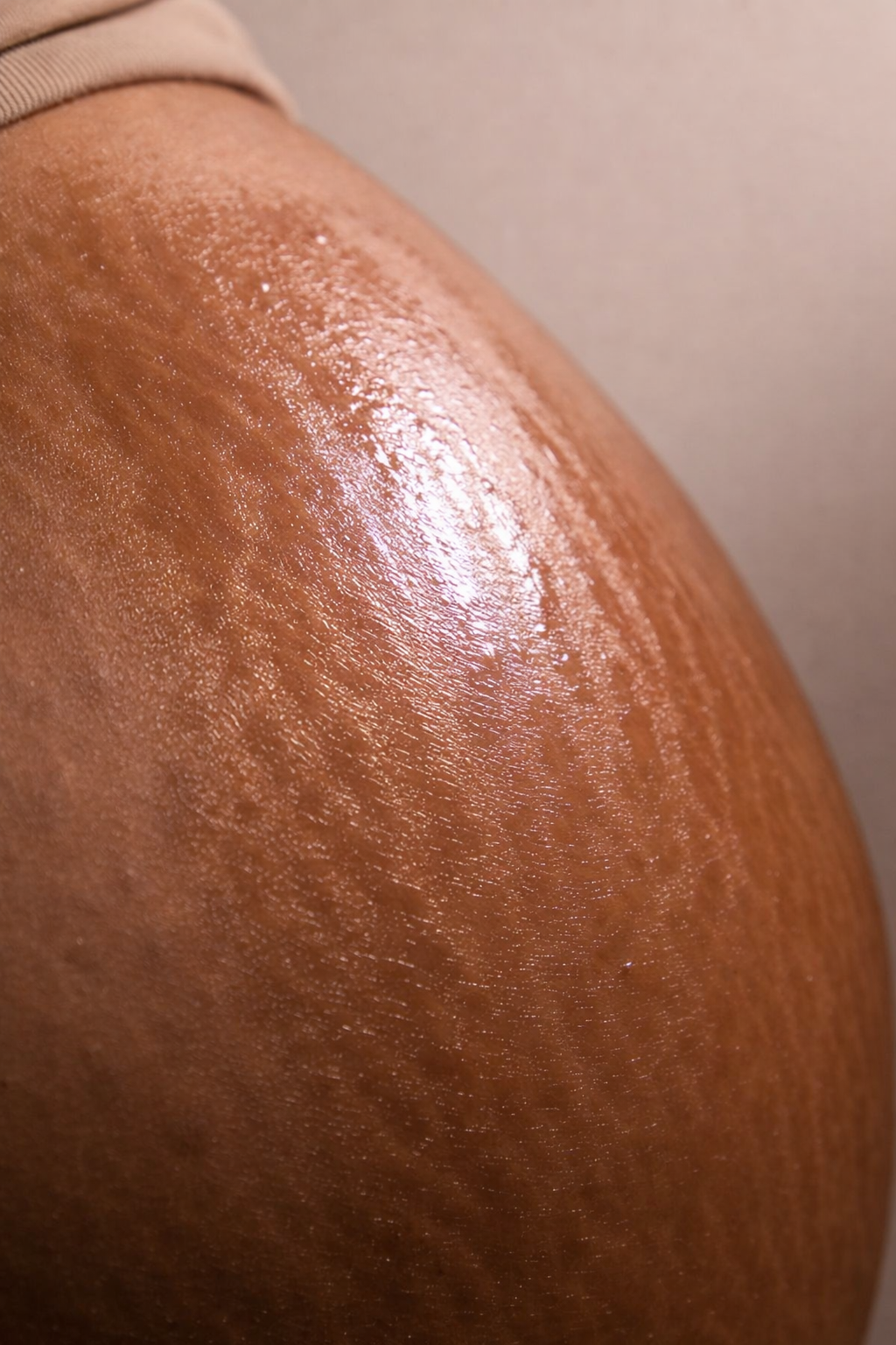 Shiny lotion on a person's pregnant belly with a neutral background