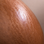 Shiny lotion on a person's pregnant belly with a neutral background